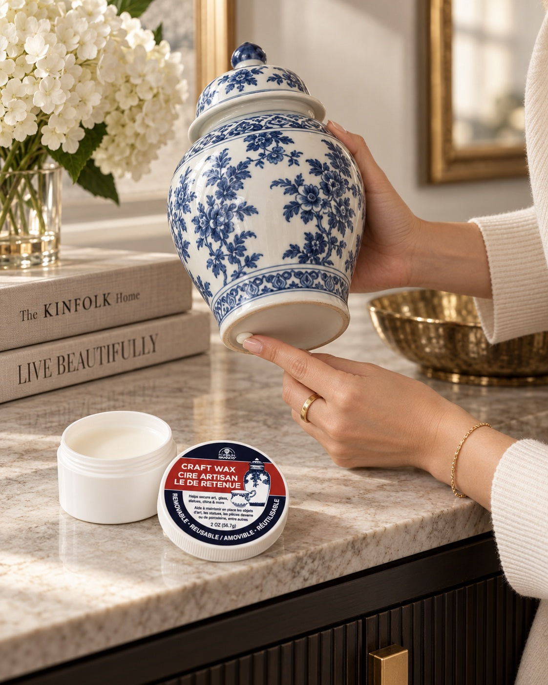 Applying a small amount of Fox Run Craft Wax beneath a blue-and-white porcelain ginger jar, with the open wax container and lid nearby.